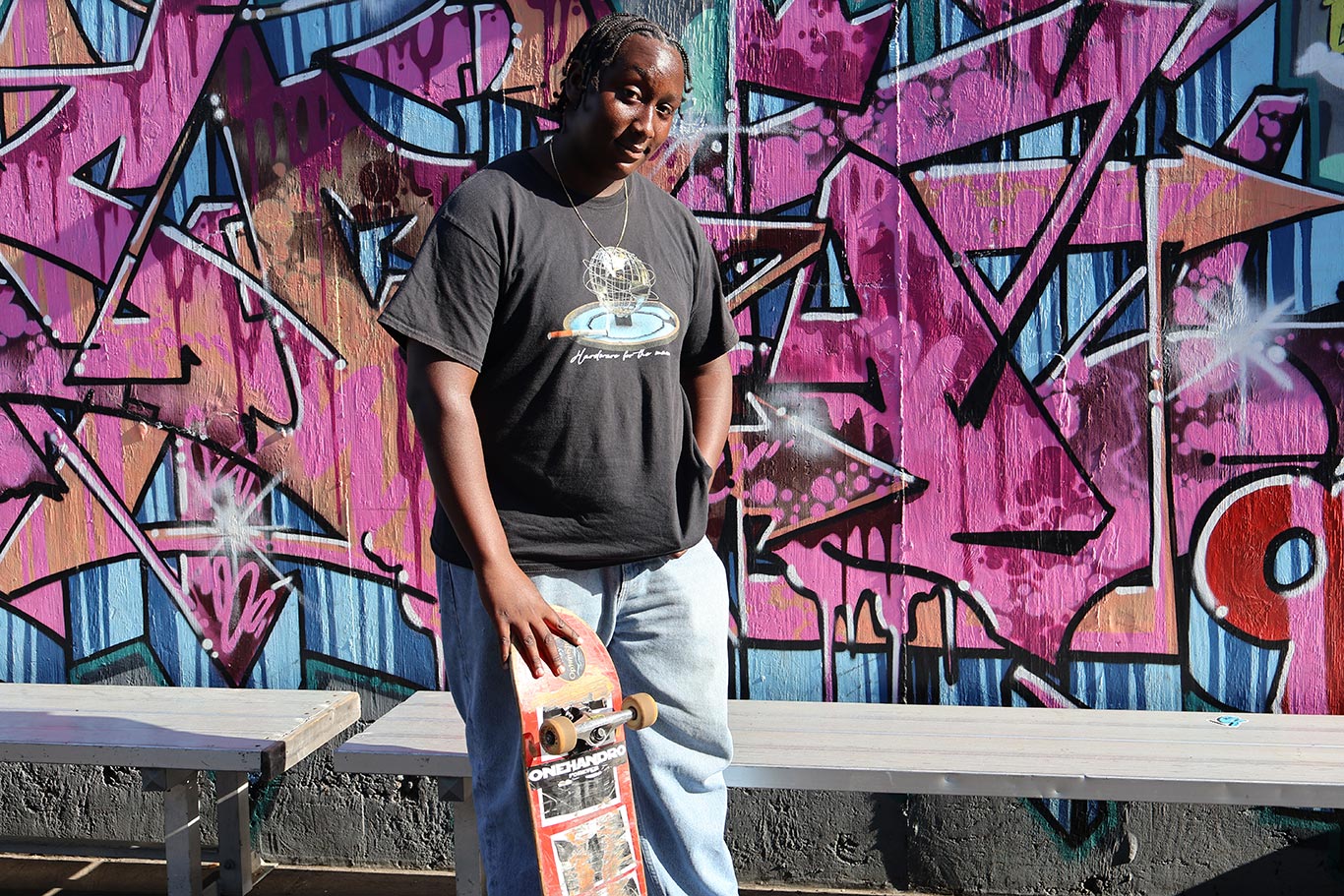 Skater in front of graffiti wall holding skateboard smiling